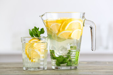 Jug and glass of tasty cold lemonade in kitchen