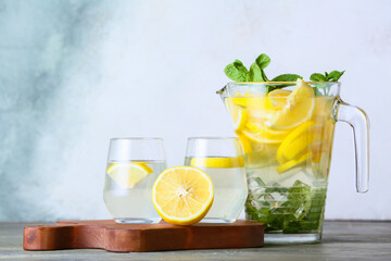 Jug and glasses of tasty cold lemonade on light background