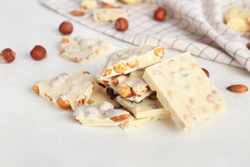 Pieces of delicious white chocolate with nuts on light background
