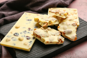 Wooden board with pieces of white chocolate and nuts on table