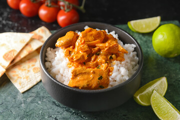 Bowl of tasty chicken tikka masala and rice on table