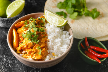 Bowl of tasty chicken tikka masala and rice on dark background