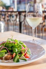 Fresh salad on a table with a glass of white wine at an outdoor cafe, with a wrought iron fence in the background. Bright cheerful image