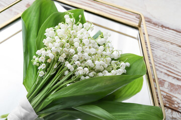 Tray with beautiful lily-of-the-valley flowers on light wooden background