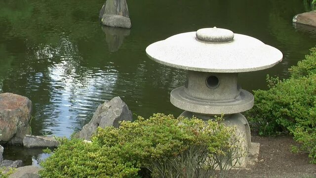 A Japanese snow lantern (yukimi doro) stands amid azalea bushes at edge of pond.