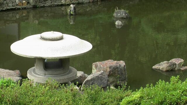 A Japanese snow-viewing lantern (yukimi doro) in front of a koi pond.