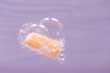 Yellow soap surrounded by soap bubbles and heart-shaped foam on a purple background. The joy and love of body care procedures.