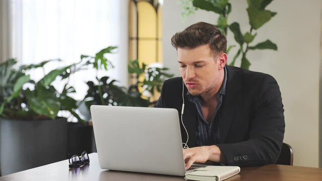 Caucasian businessman is using video call while working in green eco friendly modern working space surrounded by air purifying house plant