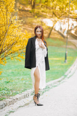 Pretty red-haired girl in a black jacket posing in the park