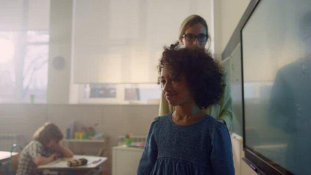 Schoolgirl writing on interactive digital whiteboard. Afro girl making task 