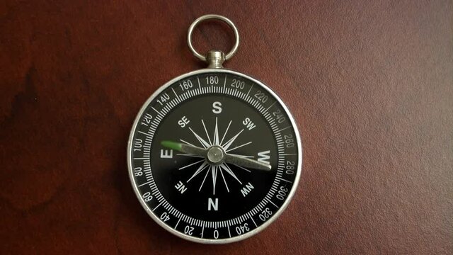Black compass on wooden table with rotating pointer. Compass show different and wrong direction.