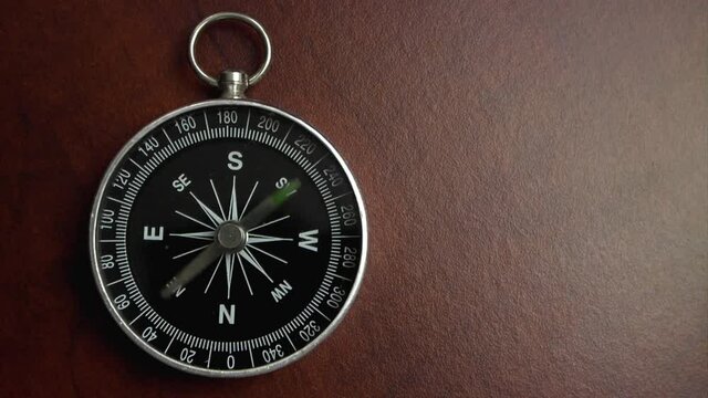 Black compass on wooden table with rotating pointer, room for text. Compass show different and wrong direction.