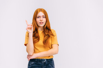 Close up portrait of charming young woman in orange t-shirt pointing with finger up, has an idea, on gray background