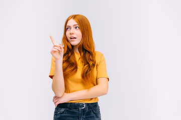 pensive girl points up with a forefinger at a blank spatial, shows a place for your advertisement or ad text
