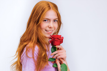 smiling cheerful redhead girl in white pink t-shirt with rose isolated on gray background in studio. People emotions lifestyle concept.