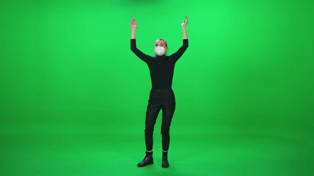 Female dancing at a concert, woman in protective medical mask at a music concert, dance and claps their hands on a green background, chromakey template, event during the coronavirus pandemic.