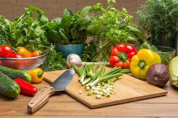 Sliced green onions, kitchen knife on cutting board. Vegetables and dill, spinach leaves and cilantro on table