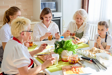Friendly caucasian family drinking tea and having happy time together, at home in kitchen, have rest after cooking, sitting at table in aprons. family consisted of females of different generations