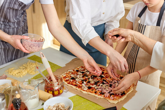 Cropped female hands adding ingredients, prepading tasty pizza for whole family. close-up photo of women at home, preparing meal, helping. concept pastimes of isolation time in quarantine mode