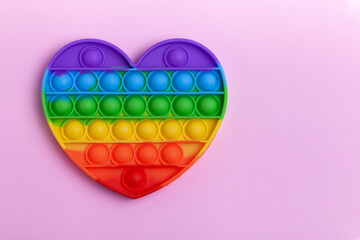 Rainbow heart shape Pop it fidget toy on pastel background. Simple dimple toy on pink pastel background.  - obrazy, fototapety, plakaty