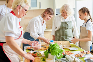 friendly family members, children and adults make pizza for family, add ingredients, copy space and lifestyle, culinary concept. Side view on caucasian happy senior ladies and granddaughters in apron