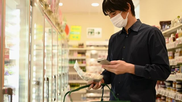 マスクをした男性がスマートフォンで食品の情報を読み取りながら買い物をしている。