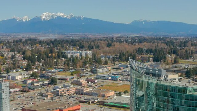 A Snow-Capped Mountain is Juxtaposed with a Modern Glass Condo Tower in Surrey, British Columbia Canada. A Cinematic Drone Orbit on a Sunny Day