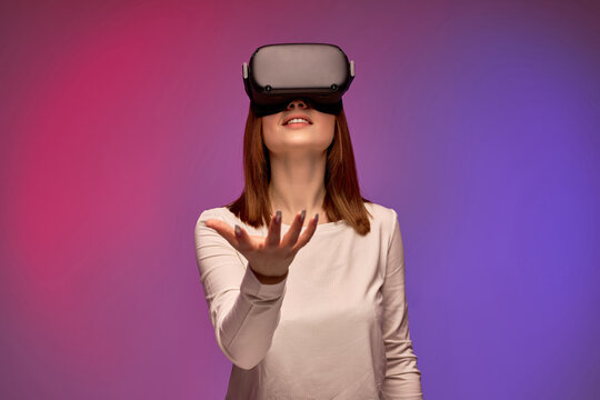 Fototapeta woman trying VR headset and exploring another world on colorful background. caucasian female using VR headset, spreading arms, looking at side. Portrait. Playing virtual game alone