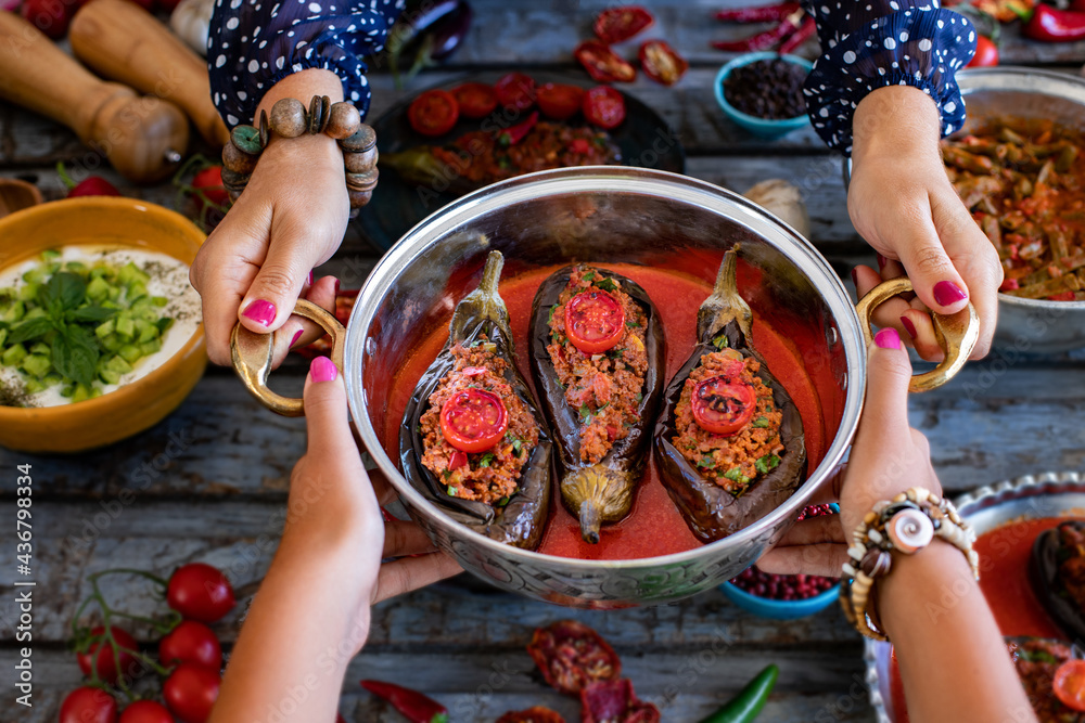 Wall mural stuffed eggplant at the hands of two women in the plate