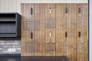 Different barbecue grids hang on wainscoting made of thin planks and elegant furniture set in...