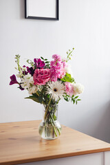 Pink and pastel white flowers in Modern glass vase on wooden table on gray wall background
