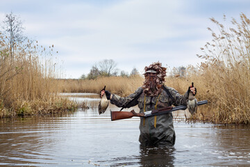 a hunter stands in the water with two dead ducks in his hands