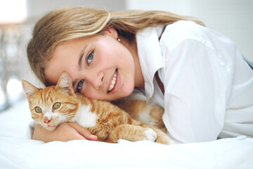 The girl is resting on the bed with her ginger kitten. A child with an animal. High quality photo.