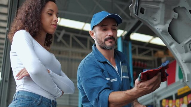 Mechanic man checking engine oil level to woman customer and discussing repairs done to her vehicle at the repair garage.
