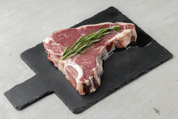 Raw t-bone steak marinated in oil on gray table