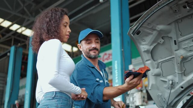 Mechanic man checking engine oil level to woman customer and discussing repairs done to her vehicle at the repair garage.