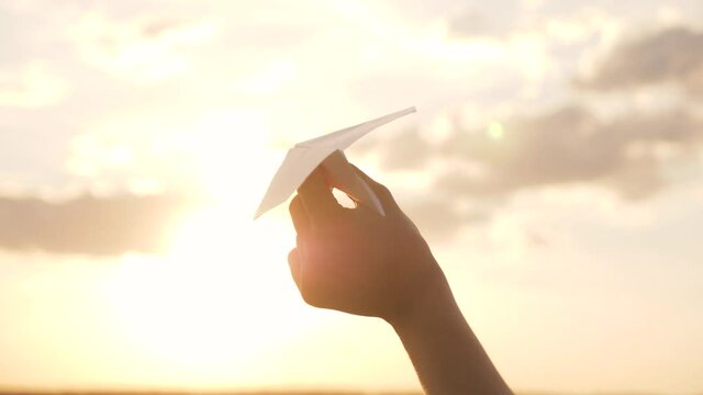 Silhouette of paper airplane in child's hand against background of sunset sky. Take off dream toy plane. Child's hand holds paper airplane in sky. Child playing in toy plane silhouette, child's dream.
