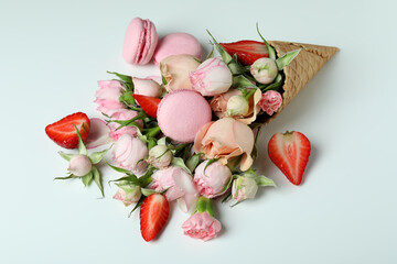 Waffle cone with flowers, strawberry and macaroons on white background