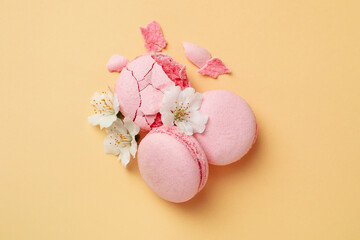 Tasty macaroons and flowers on beige background