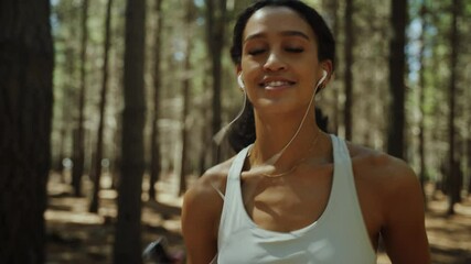 Mixed race female running in forest exercising in nature listening to music with earphones 