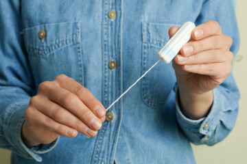 Woman in denim shirt holding a tampon, close up