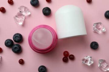 Roll-on deodorant, ice cubes and berries on pink background