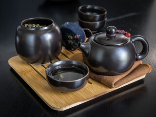 Green tea brew in a jar , black teapot , cups on a  wooden black  table .  Green tea brew in a cup .  Tea ceremony on a black background .