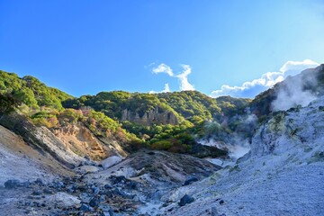 Fototapeta na wymiar 青空バックに見る晩秋の登別地獄谷と吹き上げる水蒸気の情景＠北海道