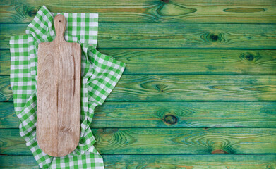 Cutting board on green checkered tablecloth, top view