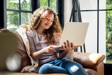 Pretty smiling Caucasian woman using laptop computer on the couch at home