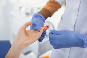 Unrecognizable female African American health worker doing a finger prick test for HIV, drawing...
