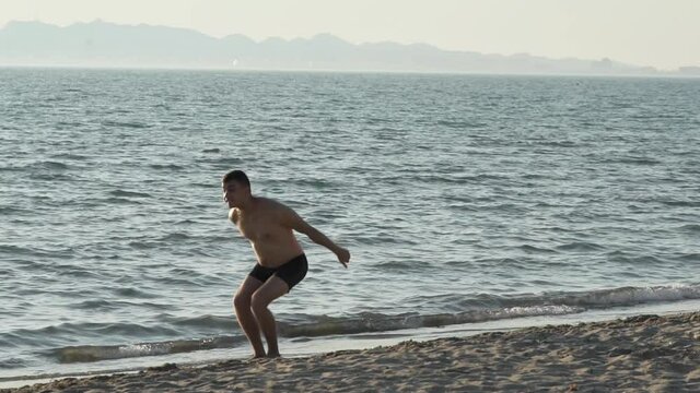 Slow motion of a young fit active gymnastic man doing a back flip on the sandy beach