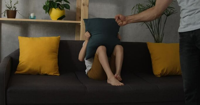 Man's hand threatens with a fist, the child hides in fear behind the pillow. Son is afraid of his father. Domestic violence. Education by force