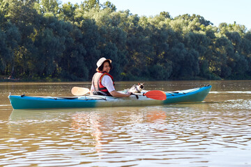 Woman rowing a blue kayak with her mekong bobtail (siames) cat at the river. Domestic lying on a kayak on the kayak
